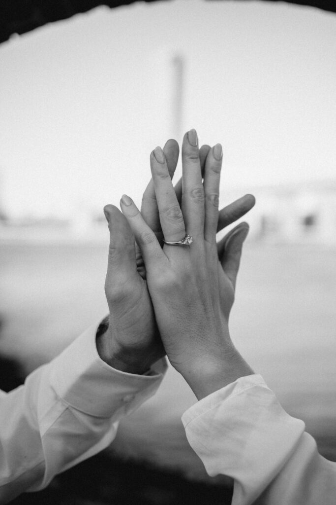 Black and white image with couples hands intertwining with beautiful engagement ring facing the camera