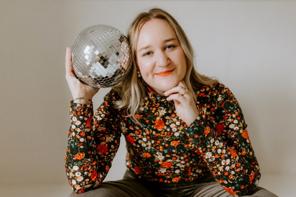 Anya Kubilus sits on floor and holds disco balls.