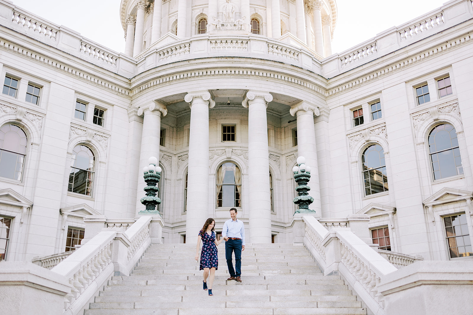 an engaged couple walks down the steps of the wisconsin capitol building in madison