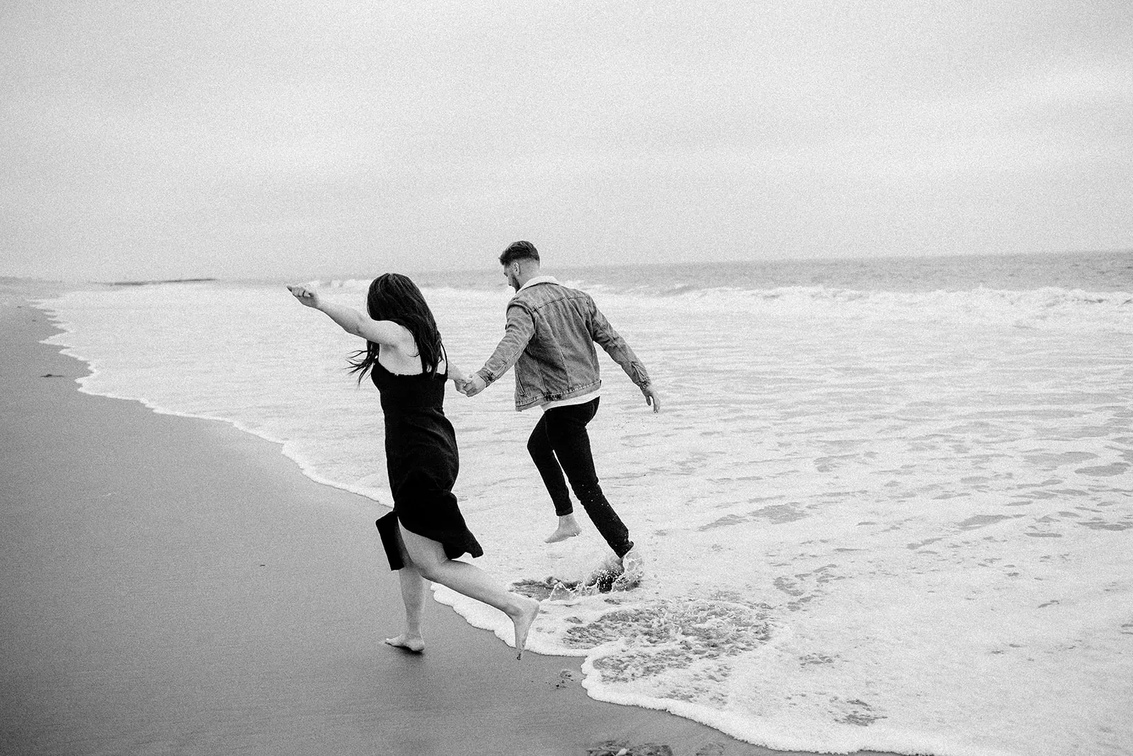 couple runs through waters of southern california beach during their engagement session