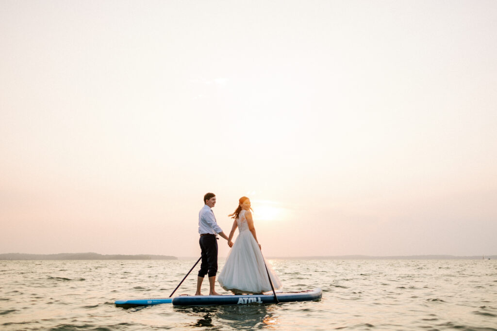 couple paddleboards on Madison, Wisconsin, lake in their wedding attire