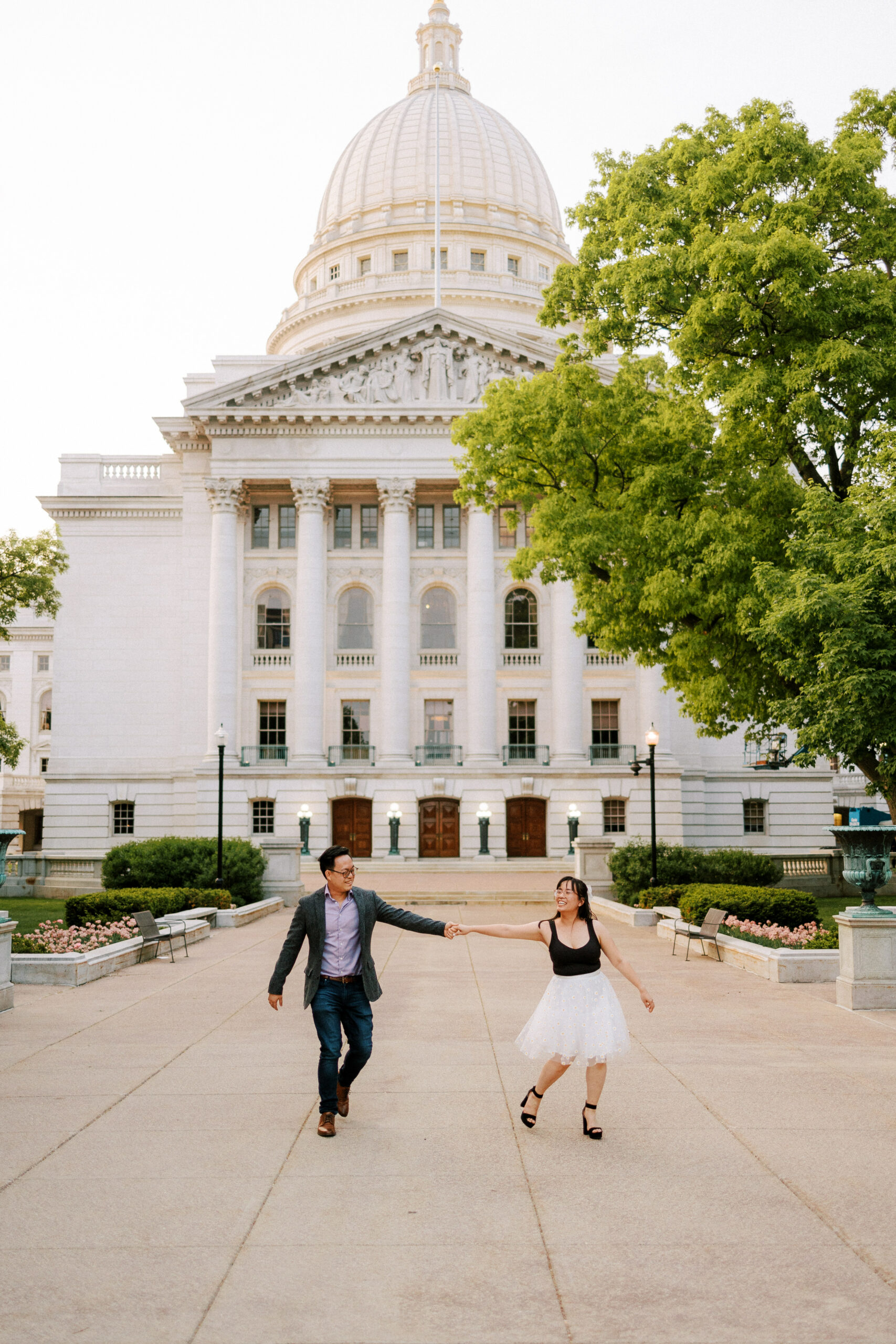 couple walks in front of capitol building in Madison wisconsin during their engagement session