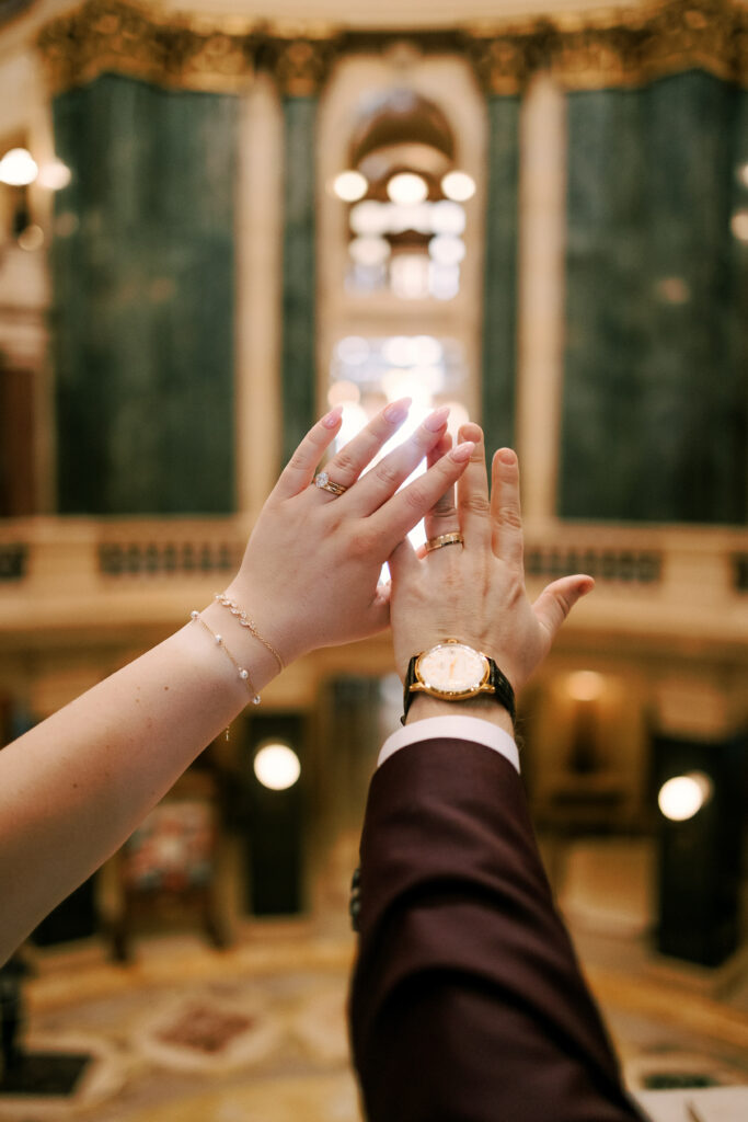 couple holds out their hands to show off their rings in the Madison Wisconsin Capitol building