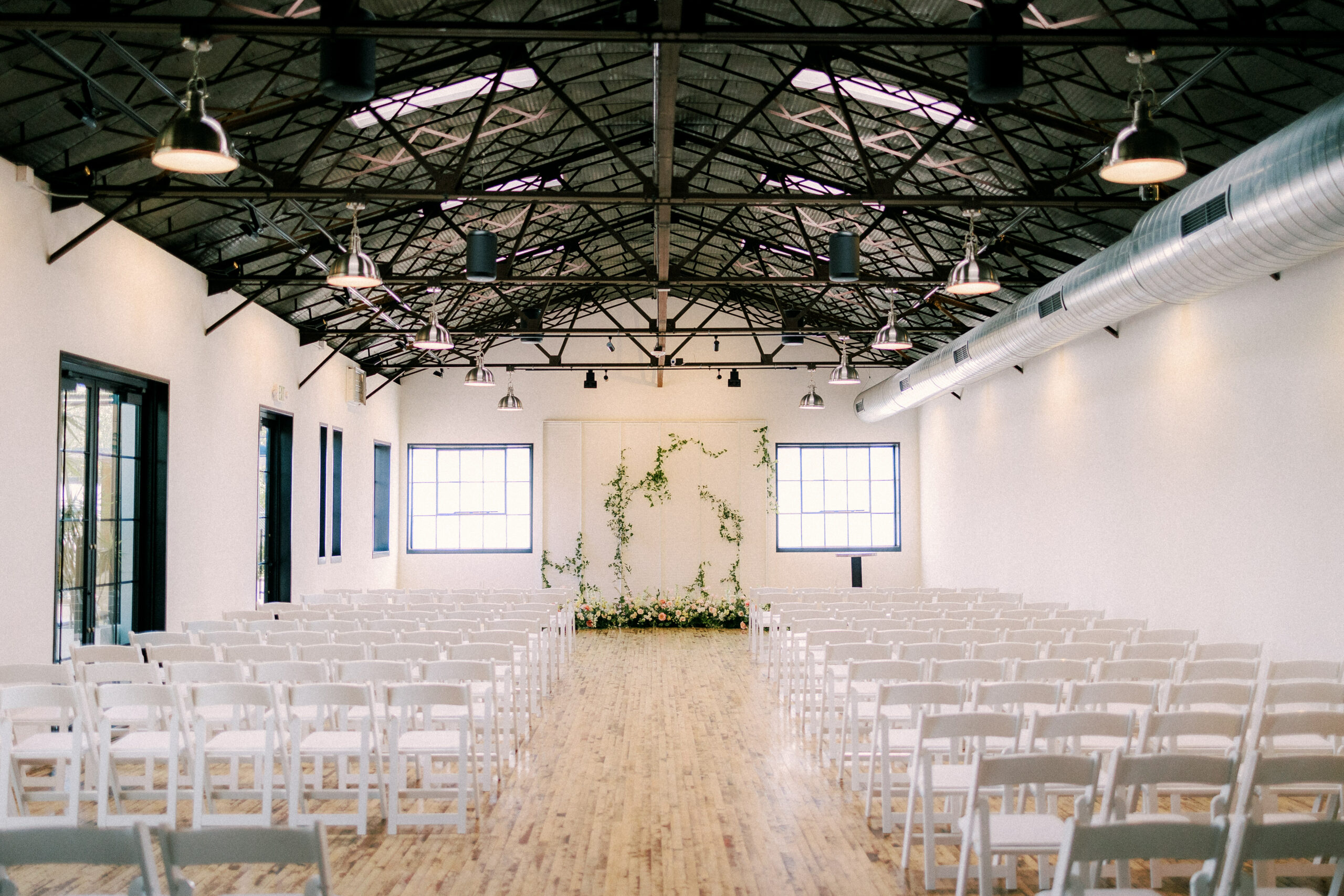 a beautiful ceremony space featuring white chairs and lovely floral on the wall at the tinsmith in madison wisconisn